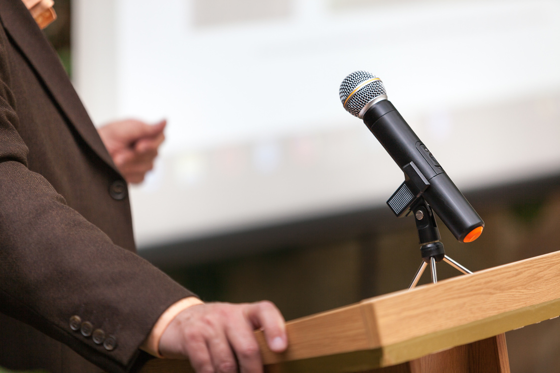 A man stands a with a microphone and holds a conference