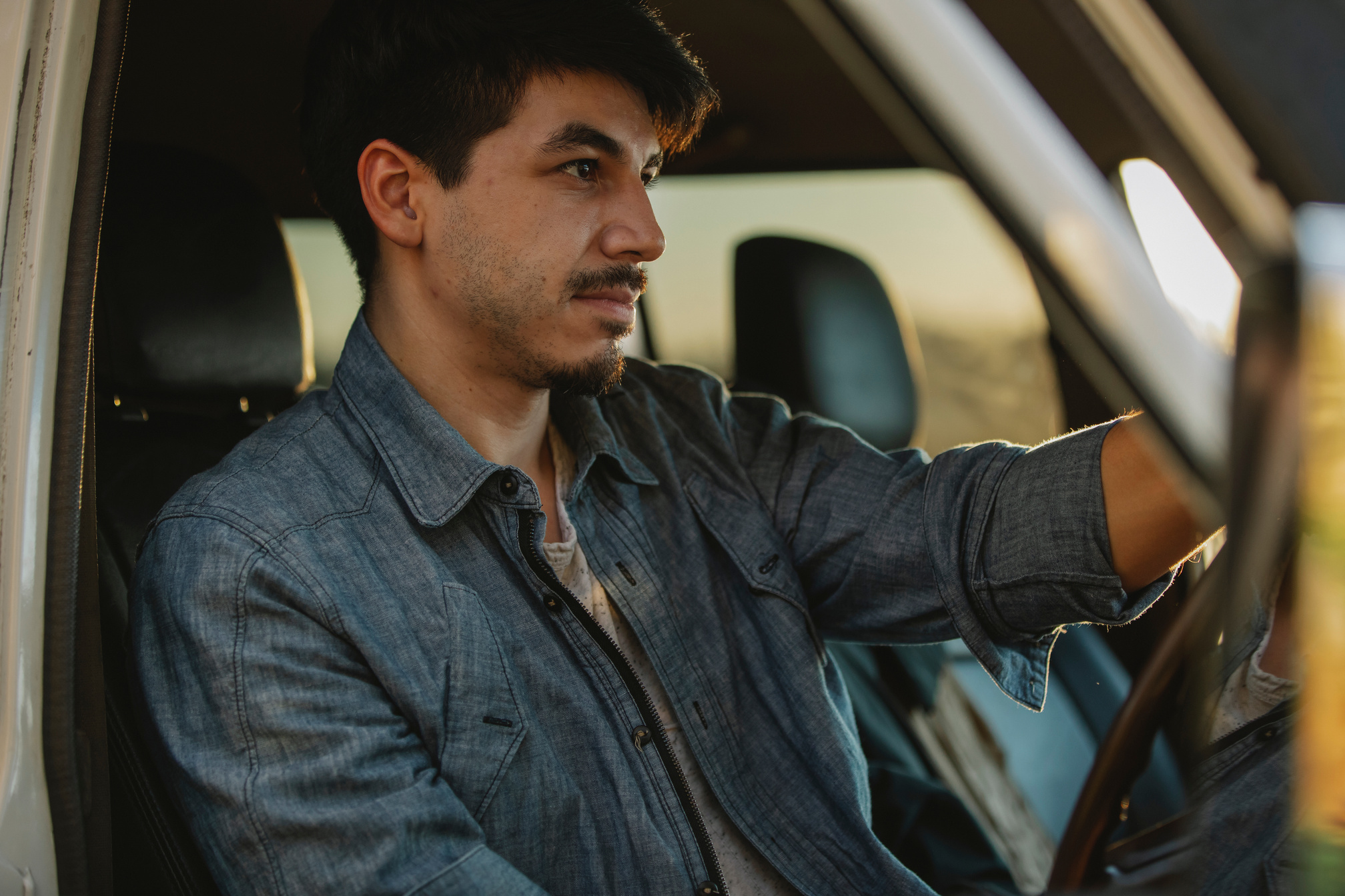 Serious young guy driving car at sundown